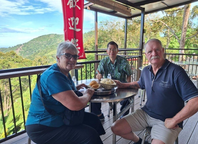 Three people seated at an outdoor table with a scenic view of hills and trees in the background. 2