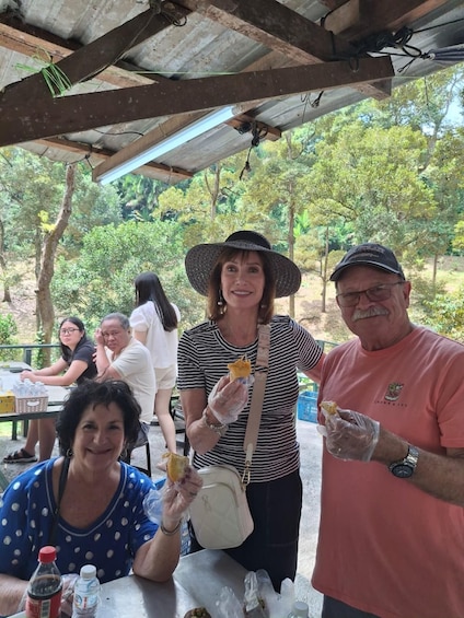 A group of people outdoors under a shelter, eating food and holding drinks. 5