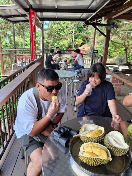 A man eating a durian at a table with a camera and a woman sitting beside him. 3