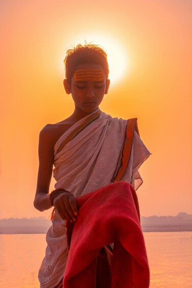 A person in traditional attire by a body of water during sunset. 2