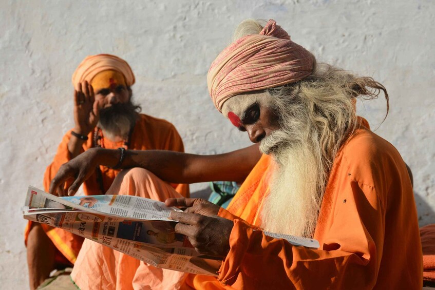 Two individuals in orange robes reading a newspaper. 3