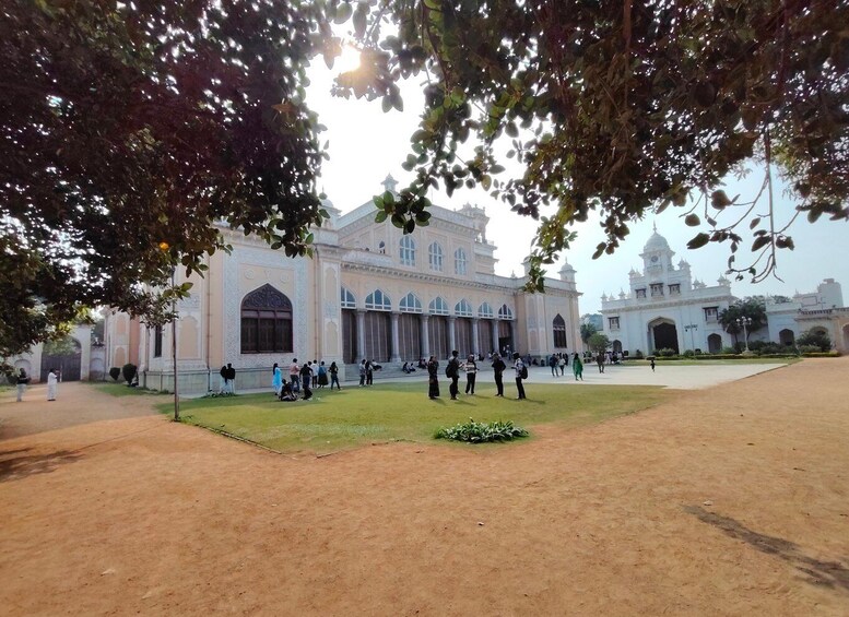 A large, ornate building with multiple domes and arches, surrounded by a spacious courtyard with people walking and sitting. 1