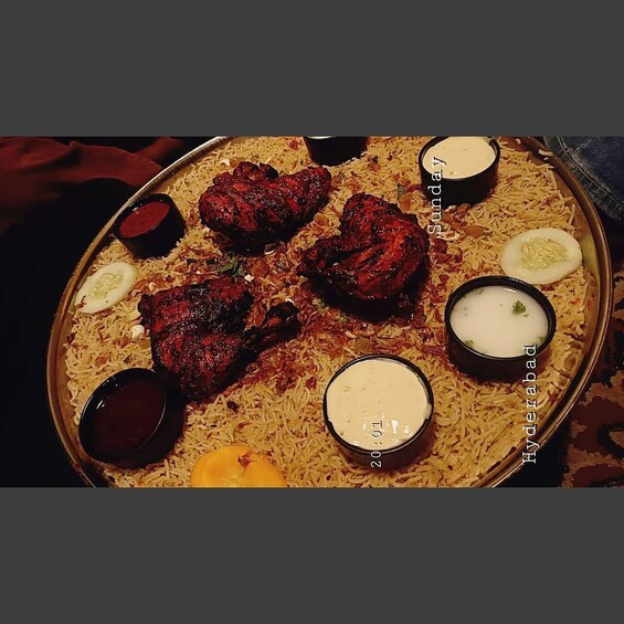 A platter of biryani with meat, garnished with slices of cucumber and a boiled egg, accompanied by two types of raita. 2