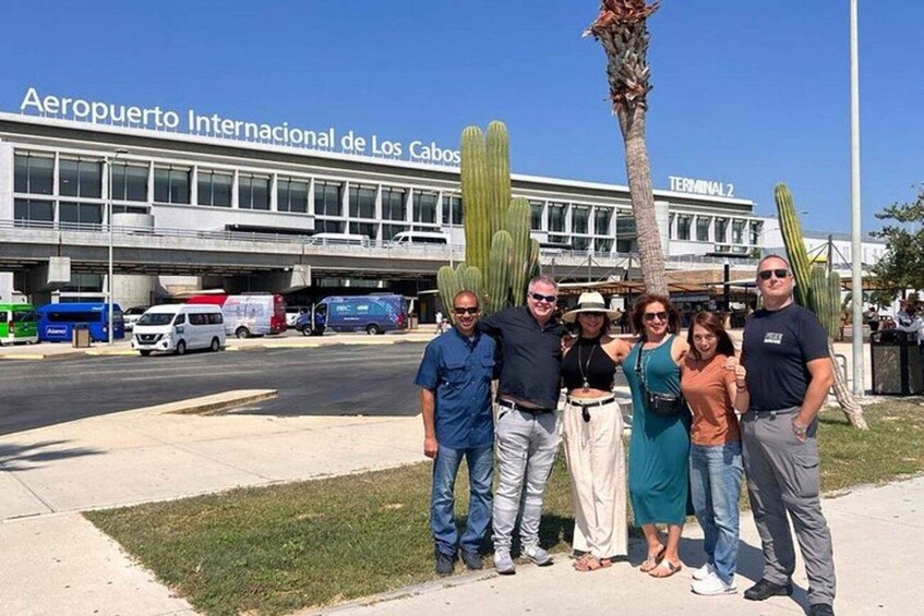 A group of people standing in front of the Aeropuerto Internacional de Los Cabos building. 2