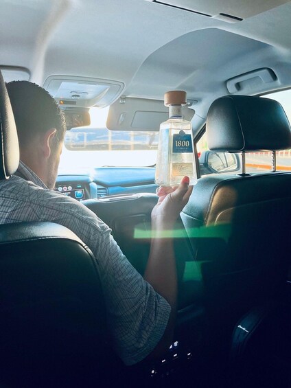 A person holding a bottle of 1800 tequila in a car. 3