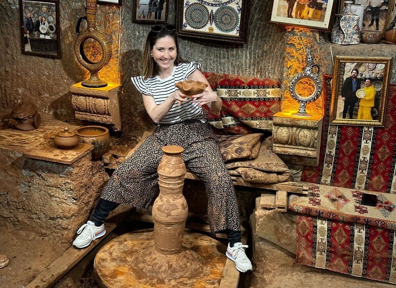 A person sitting on a pottery wheel in a workshop filled with pottery items and decorative plates. 2