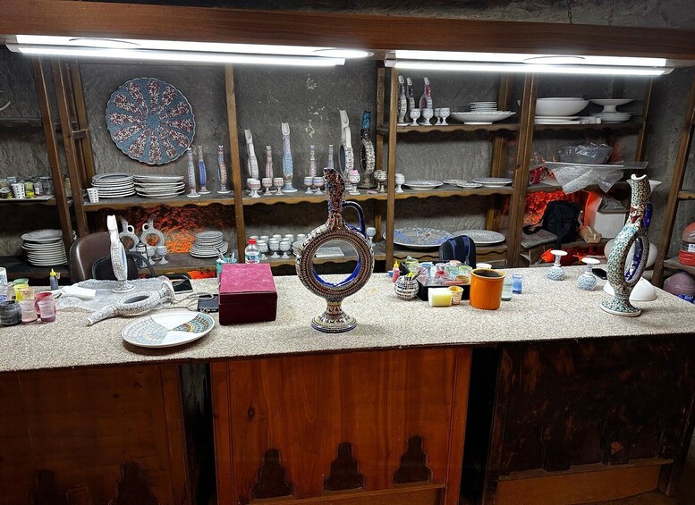 A cluttered workshop with various pottery items, including plates, bowls, and vases, displayed on shelves and counters. 4