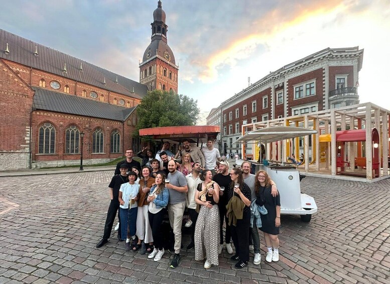 A group of people posing in front of a historic building with a clock tower, a covered market stall, and a tram. 1
