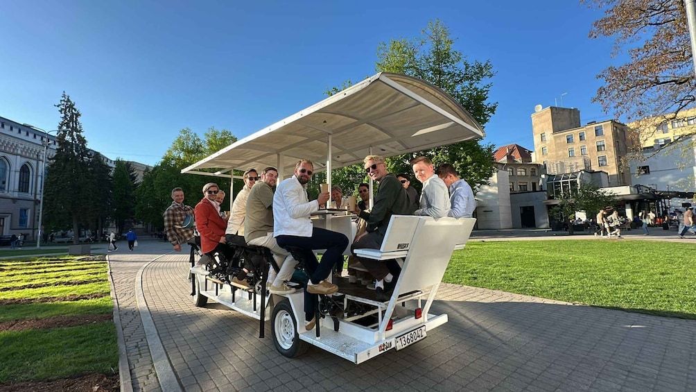 A group of people on a stationary, open-top vehicle with a canopy, parked on a paved area with grass and trees in the background. 4