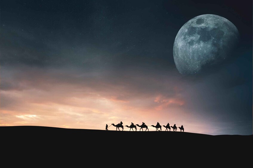 A group of people on camels silhouetted against a moonlit sky. 1