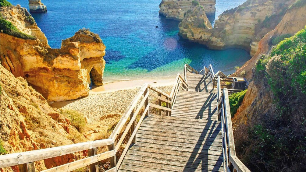 Una escalera de madera que conduce a una playa con aguas azules cristalinas y acantilados rocosos. 4