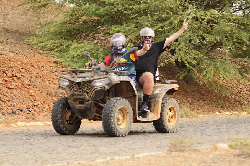Two people on an ATV on a rocky road with trees in the background. 3