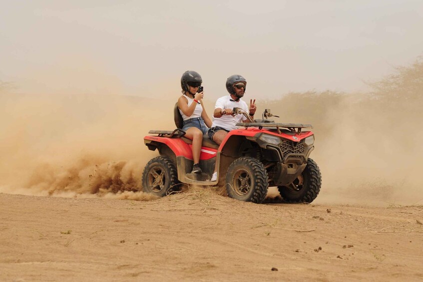 Two people on a red ATV in a dusty, open landscape. 5
