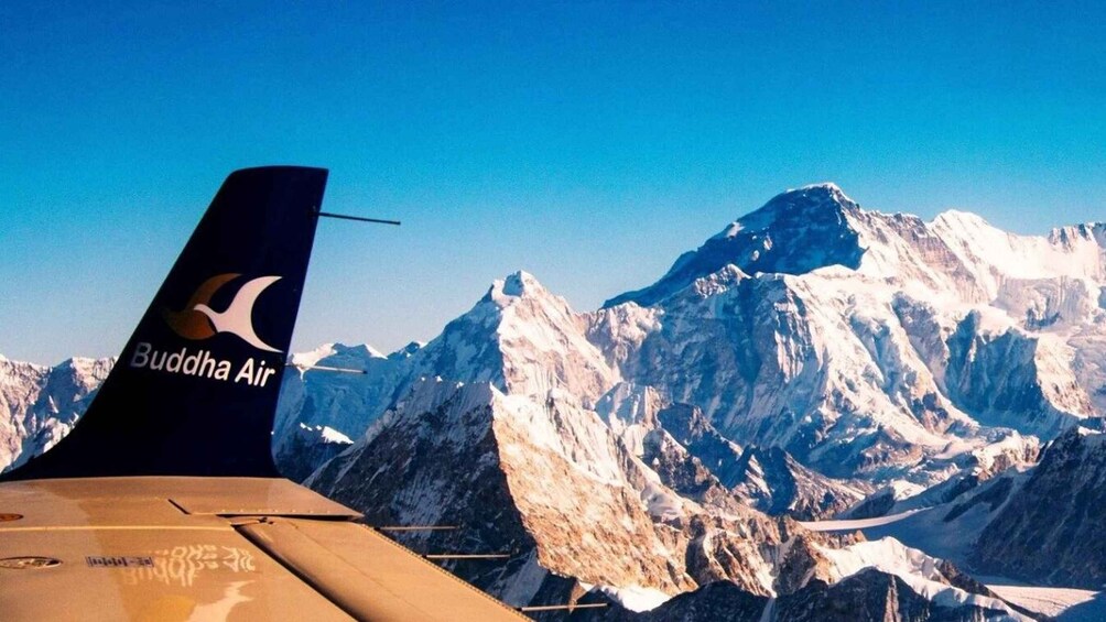 A plane's wing with the Buddha Air logo, flying over snow-capped mountains. 1