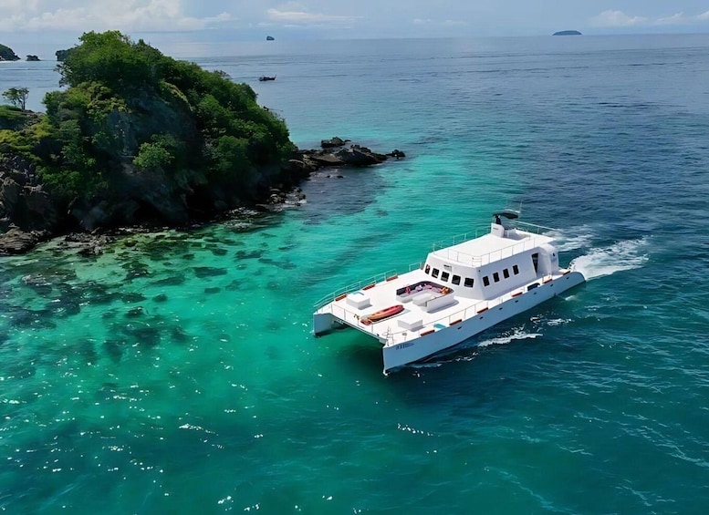 A white boat on turquoise waters near a rocky island with lush greenery. 1
