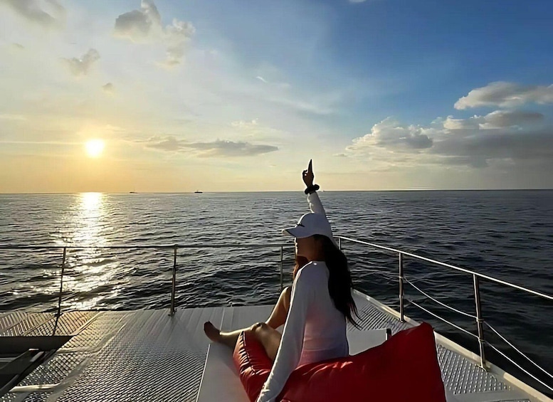 A person sitting on a boat deck during sunset, pointing towards the horizon. 2