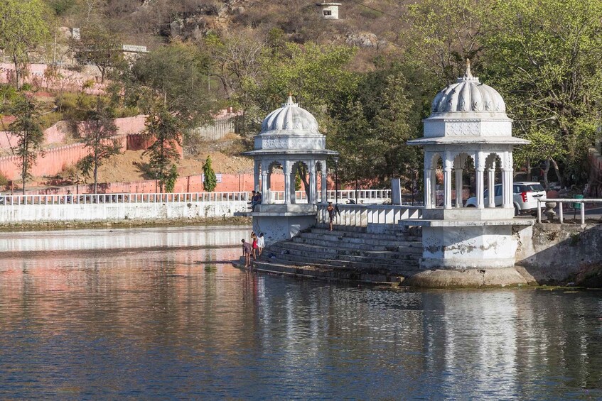 A water body with two white domed structures, a bridge, and a hill with sparse vegetation in the background. 3