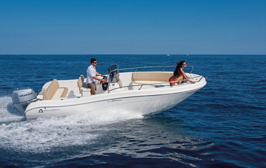 A white motorboat with two people on board, moving through calm blue waters. 2