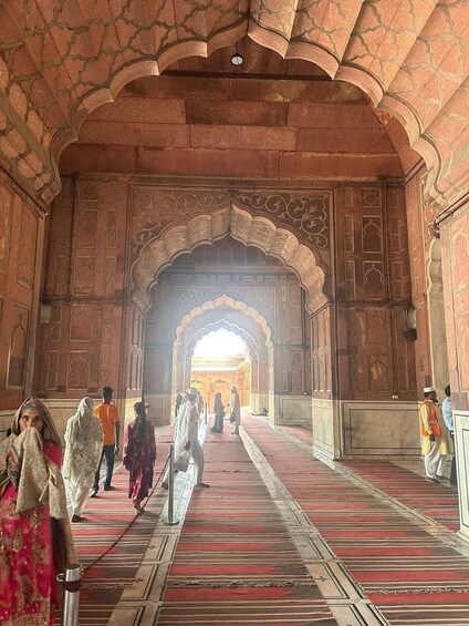 An ornate corridor with arches and intricate wall designs, leading to a bright interior space. 5