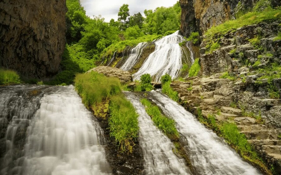 A multi-tiered waterfall surrounded by lush greenery and rocky terrain. 2