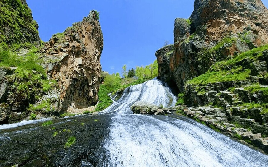 A waterfall cascading down a rocky gorge surrounded by lush greenery. 3