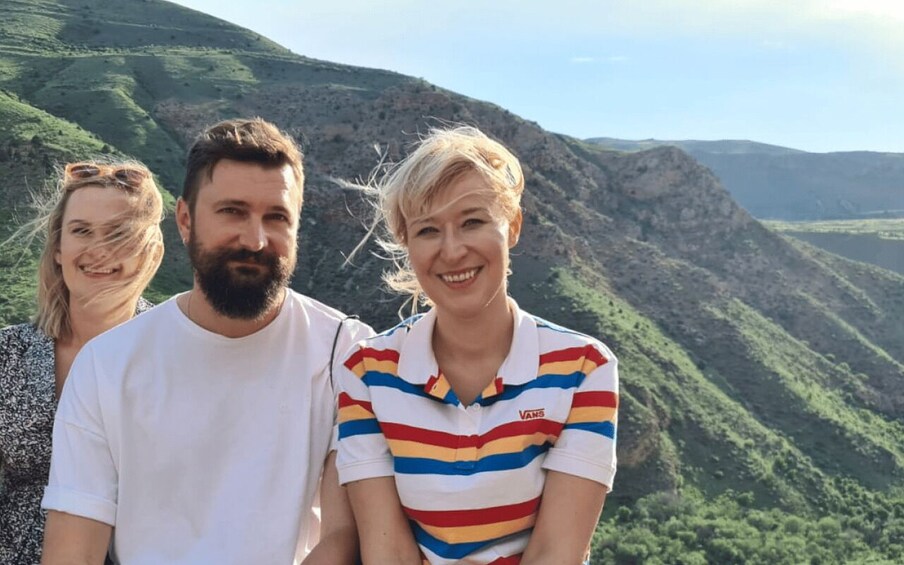 Three people standing in a mountainous area with green hills in the background. 4