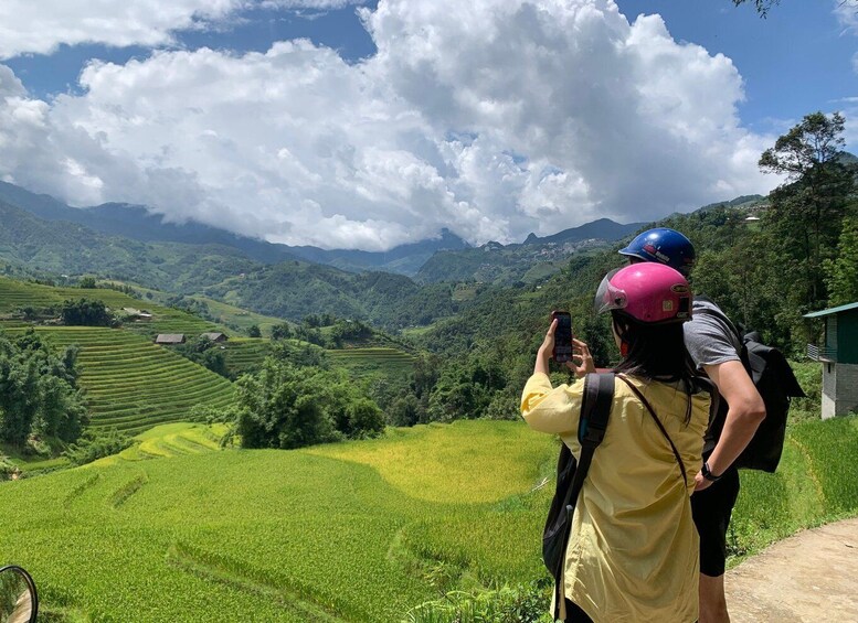 A person taking a photo of a green landscape with terraced fields and mountains in the background. 4