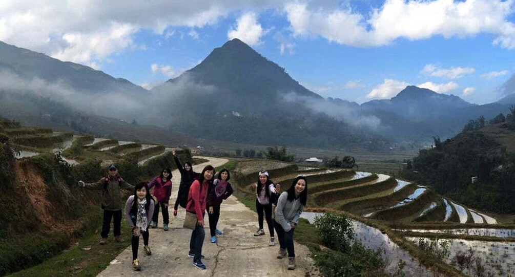 A group of people standing on a path with terraced fields and a mountain in the background. 1