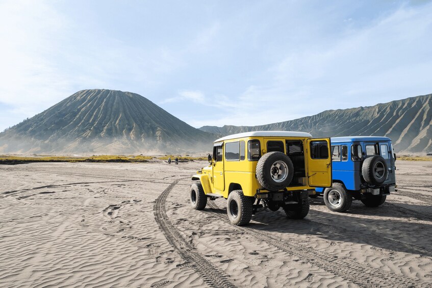 Two off-road vehicles on a sandy terrain with footprints and a mountain in the background. 2