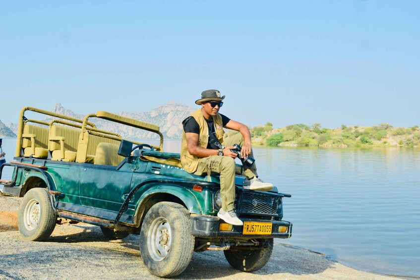 A person sitting in a green off-road vehicle by a calm river with mountains in the background. 5