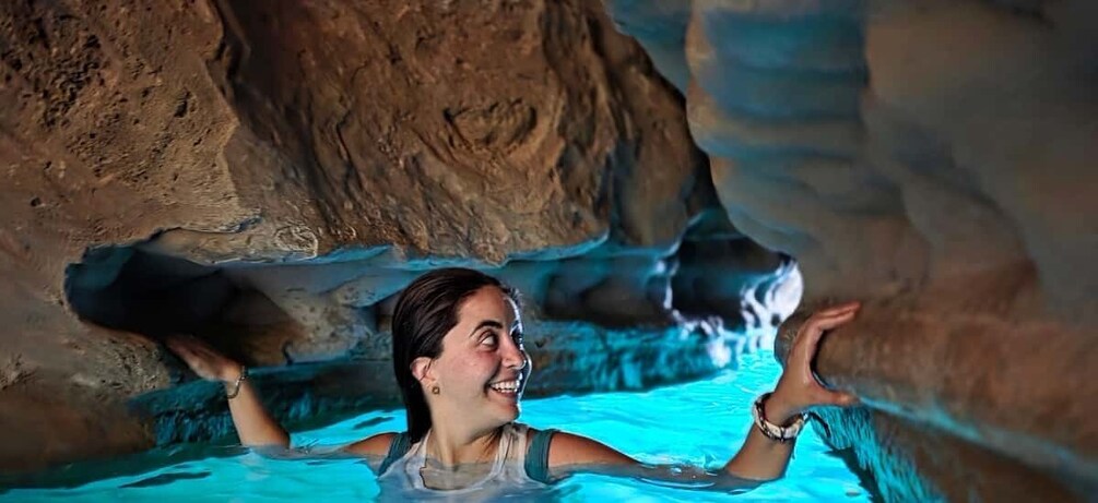 A person swimming in a pool with a cave-like rock formation in the background. 1