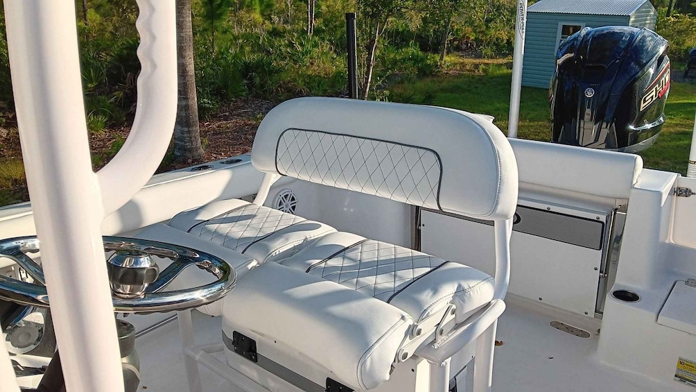 A boat's interior with a cushioned seat, steering wheel, and a small table. 4