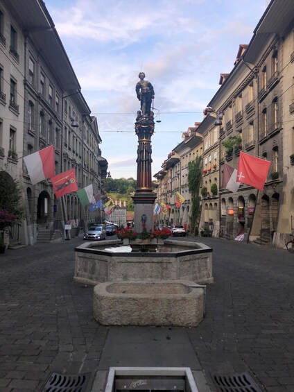 A central fountain with a statue, surrounded by buildings with flags. 2
