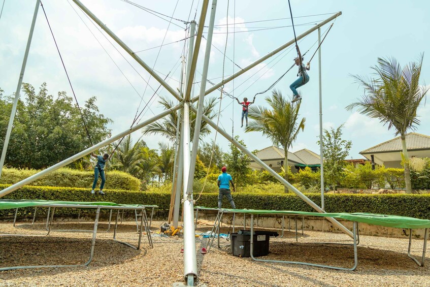 A person zip-lining, another on a trampoline, and a third preparing to zip-line, with palm trees and buildings in the background. 5