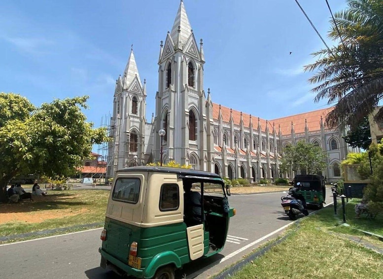A green and beige auto-rickshaw parked on a road with a large church in the background. 4