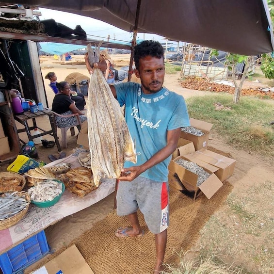 A man holding a large dried fish at a market stall. 5