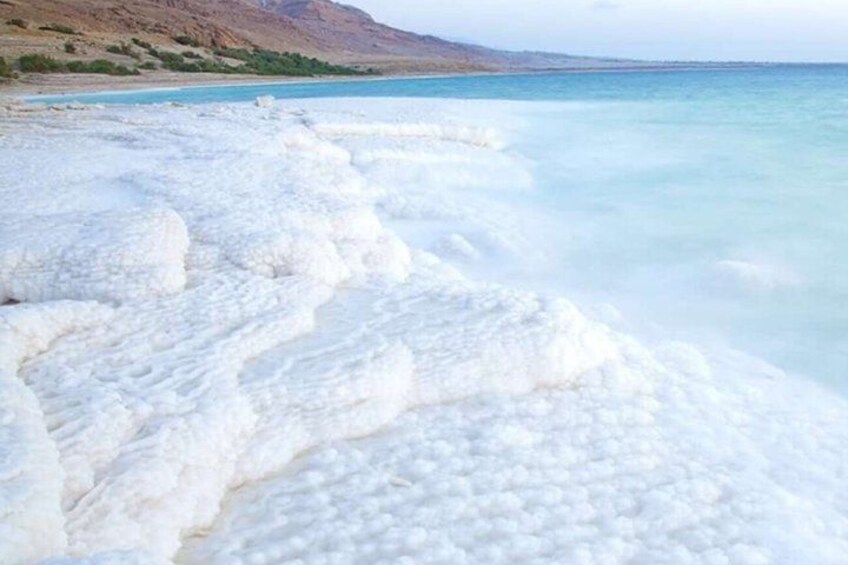 A white travertine formation along a coastline with clear blue water and distant hills. 2