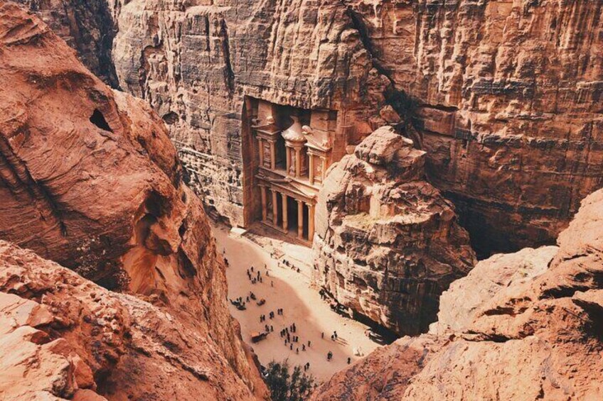 A rock-cut architectural structure in a canyon with a group of people below. 1