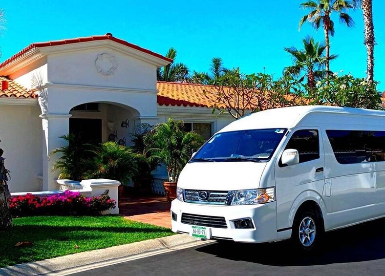 A white van parked in front of a white house with a red-tiled roof, surrounded by palm trees and tropical plants. 3
