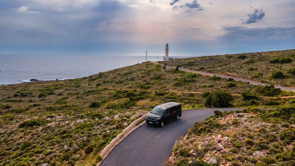 A van on a winding road in a hilly area with a lighthouse in the distance. 1