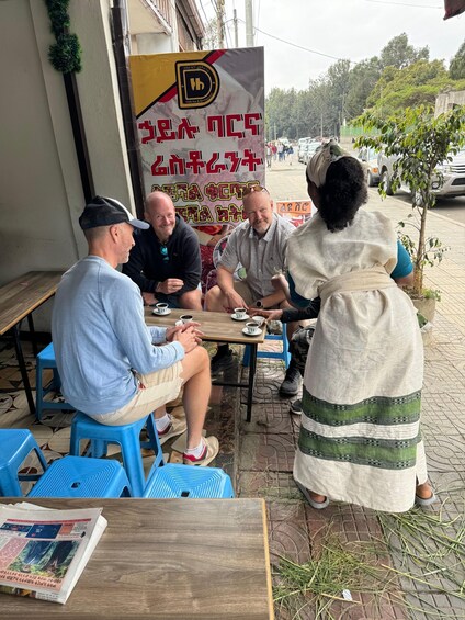 Four people sitting at a wooden table outdoors, with a banner in the background. 3