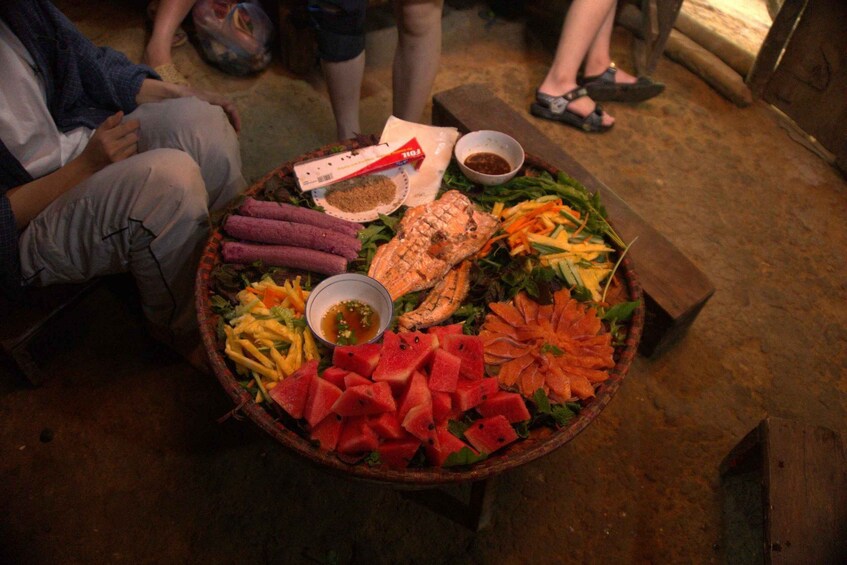 A round wooden table with various foods including watermelon, carrots, and a grilled fish. 2
