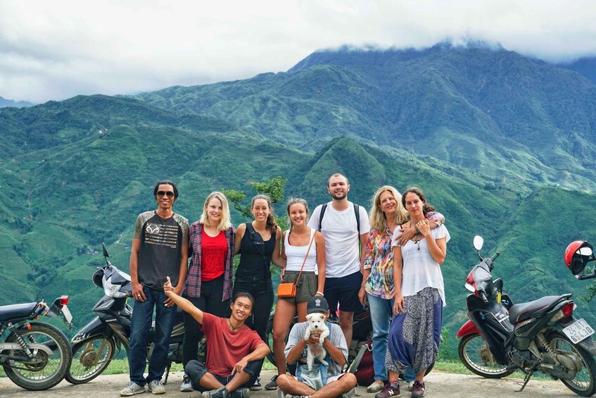 A group of people standing in front of a mountainous landscape with motorcycles parked nearby. 1