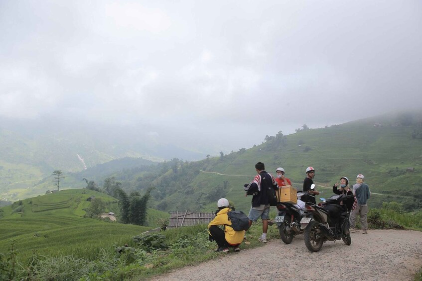 A group of people on a dirt road with a motorcycle, surrounded by green terraced fields and hills in the background. 4
