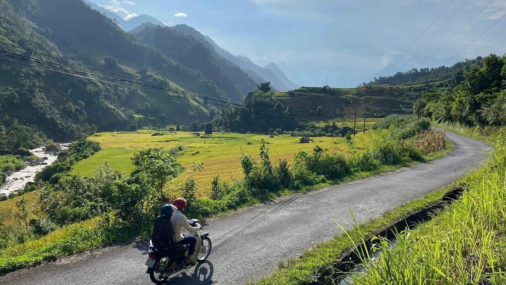 A motorcycle on a winding road with a river and fields in the background. 3