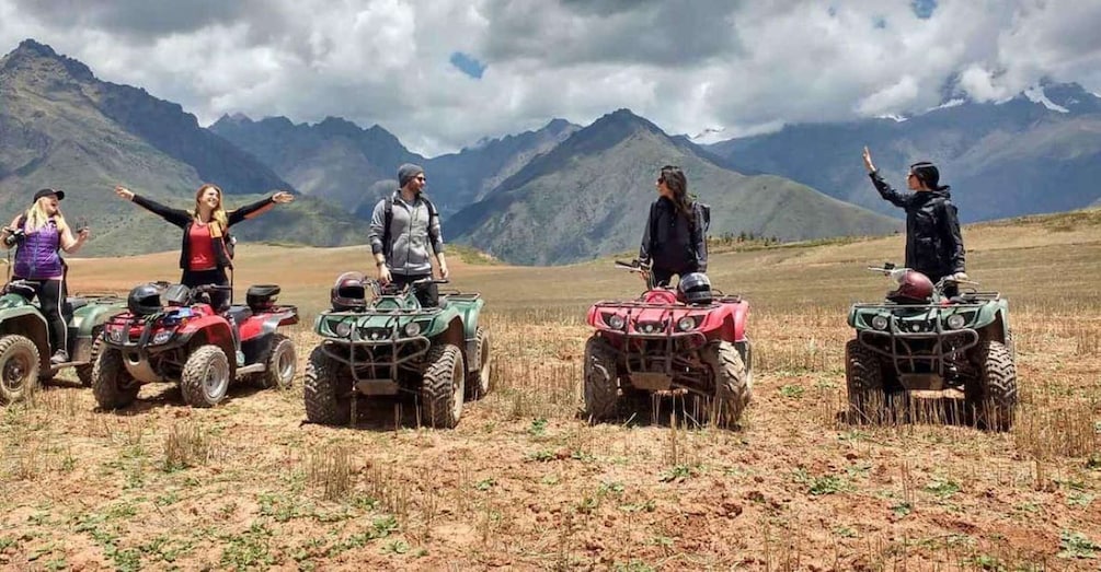 Four people on ATVs in a field with mountains in the background. 1