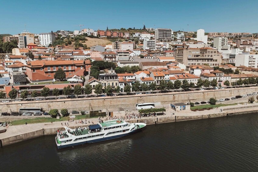A river with a boat docked at a pier, surrounded by a densely built urban area with various buildings and a hilly backdrop. 5