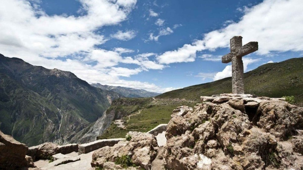 A stone cross on a rocky outcrop with a mountainous landscape in the background. 2