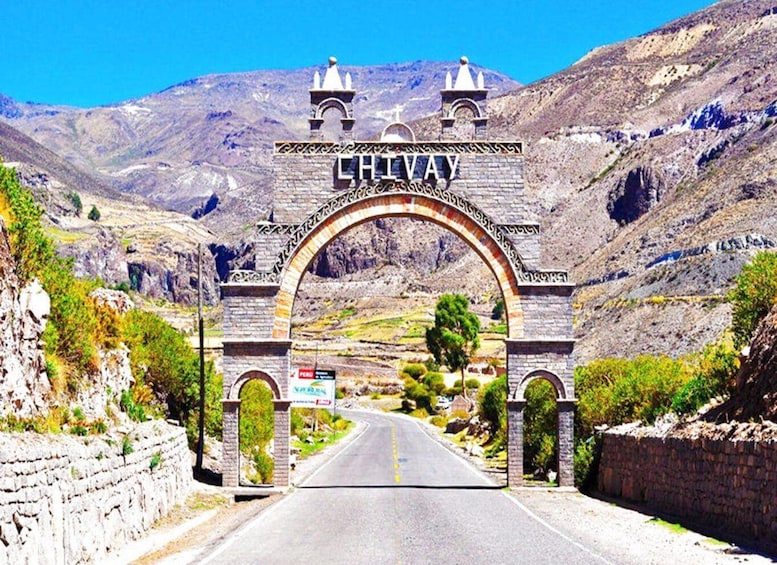 A stone archway with 'CHILVA' inscribed above a road, surrounded by mountains and greenery. 3