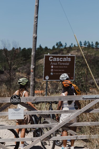 Two cyclists at a wooden fence with a sign reading "Cascals Area Florestal" and another sign indicating "Access limited to authorized vehicles." 1